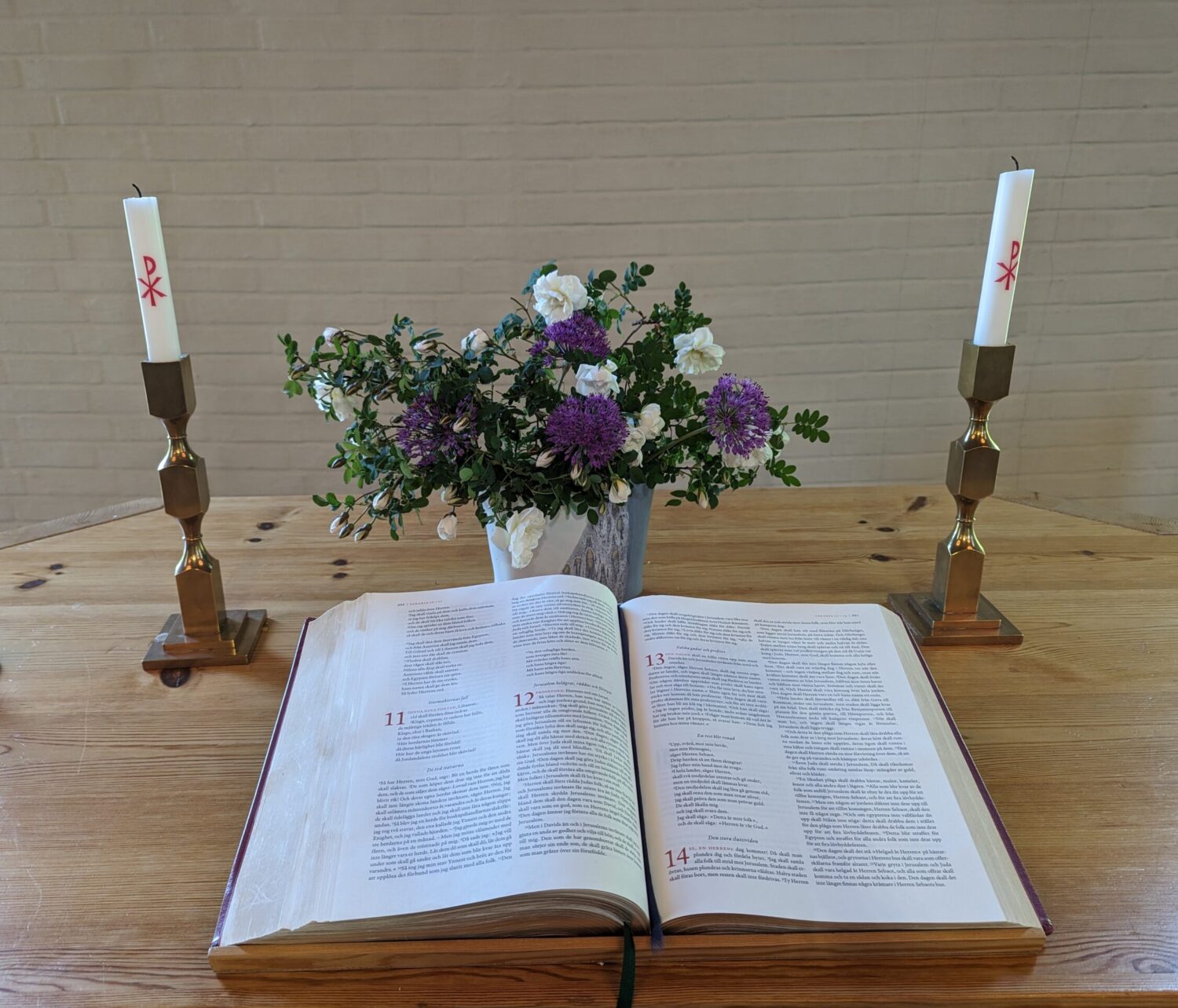 Altarbordet med uppslagen bibel, två ljus och blommor i en vas.