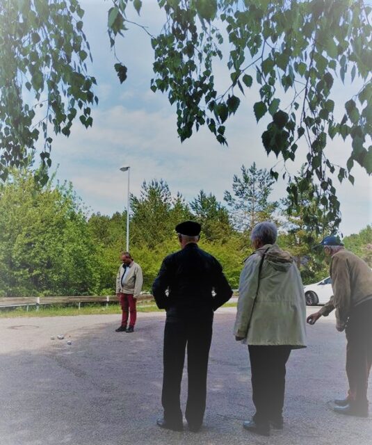 Tre personer spelar boule på kyrkans parkeringsplats, en person tittar på.