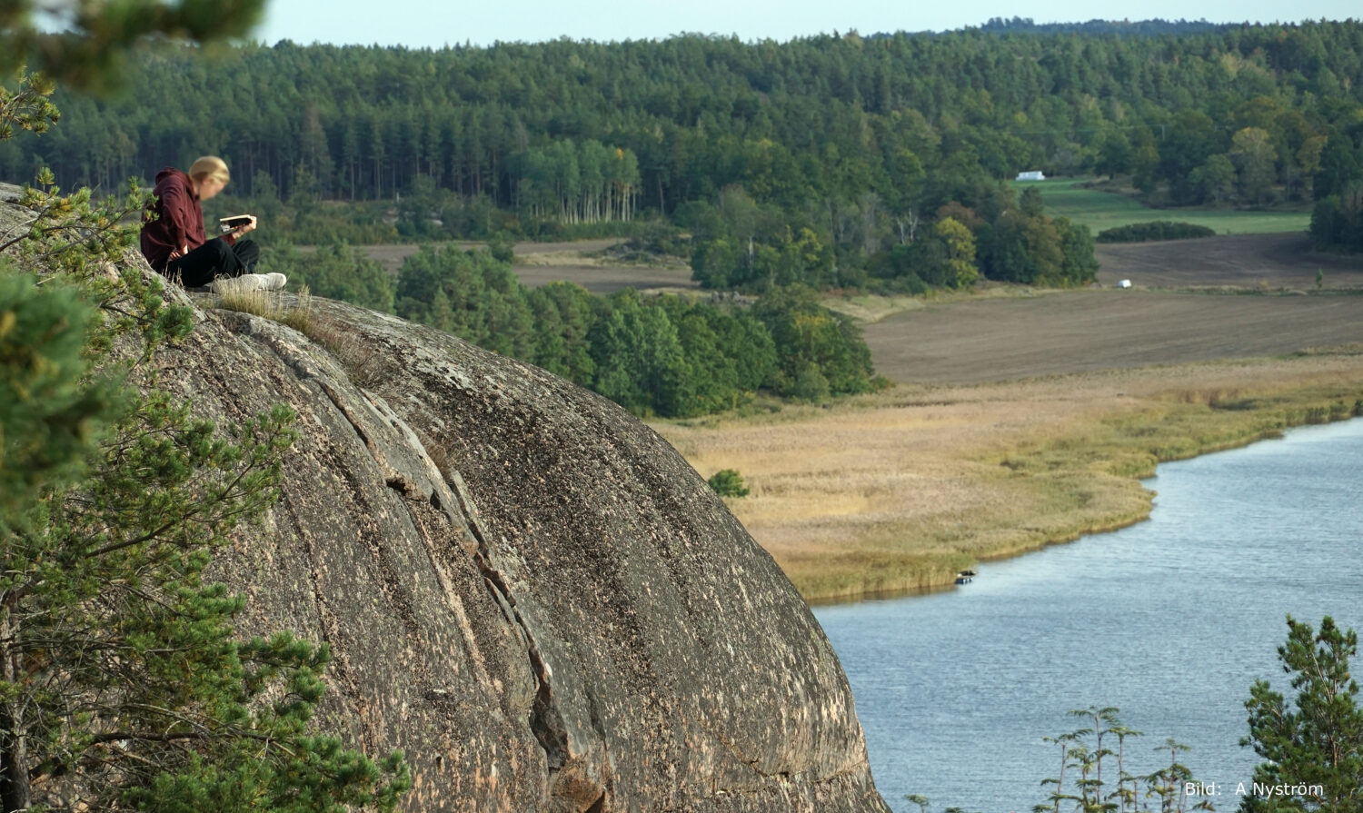 Man som sitter och läser på en hög utsiktspunkt