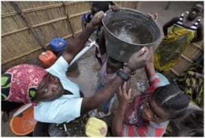 En kvinna får hjälp av en annan kvinna för att lyfta upp vattenhinken på huvudet, Malawi.