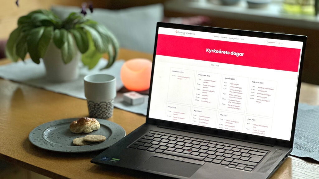 Bord med kaffekopp, fika och en laptop med webbsida som visar kyrkårets söndagar